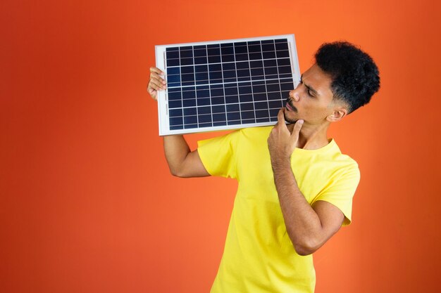 Black Man Holding a Piggy Bank e pannello solare isolato su Orange Uomo in una camicia gialla per affari Giorno dell'indipendenza