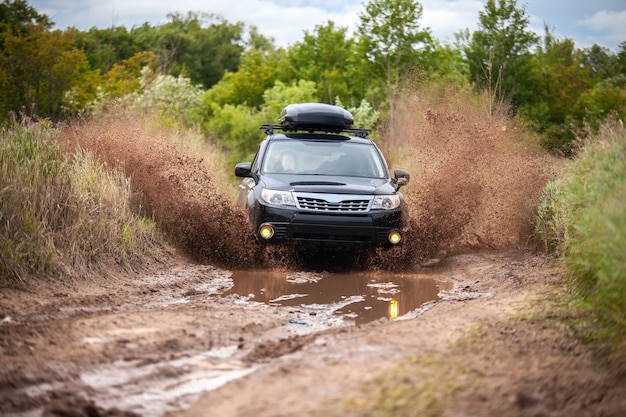 Black Subaru Forester si muove su una strada forestale sporca facendo molti spruzzi d'acqua