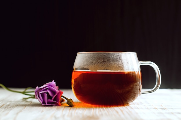 Black tea in a transparent cup next to purple flower