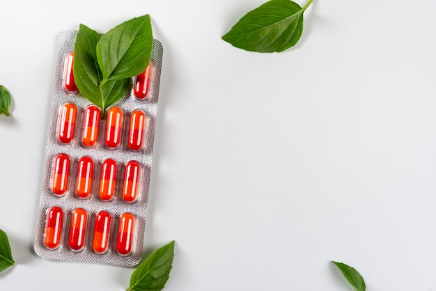 Blister con pillole rosse e foglie verdi su sfondo bianco salute e natura vista dall'alto copia spazio