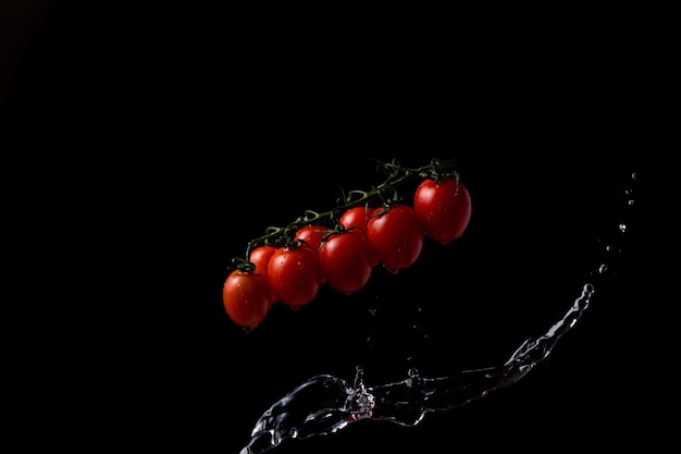 Blocca il movimento. Pomodorini su sfondo nero con spruzzi d'acqua