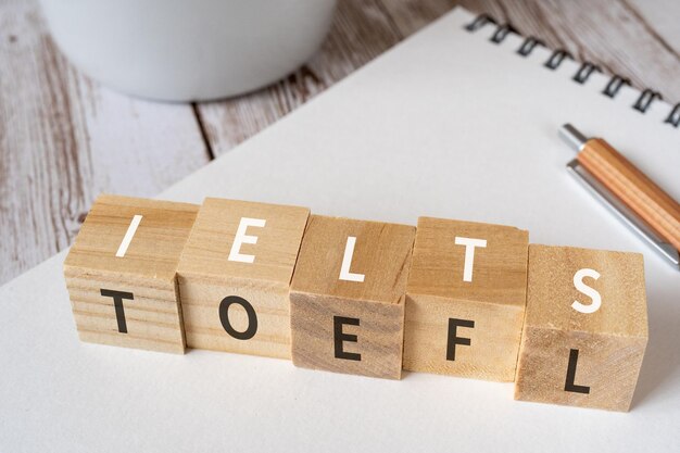 Blocchi di legno con testo concettuale IELTS e TOEFL, una penna, un taccuino e una tazza.