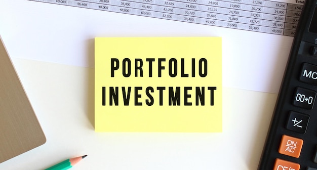 Blocco note con il testo PORTFOLIO INVESTMENT sul desktop vicino alla calcolatrice del laptop