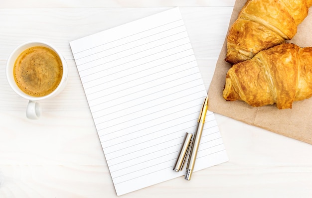 Blocco note con tazza di caffè e croissant sul tavolo Vista dall'alto