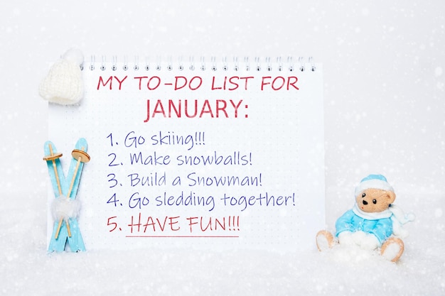 Blocco note con una lista di cose da fare sciare fare palle di neve fare un pupazzo di neve slittino divertendosi e un orsacchiotto giocattolo