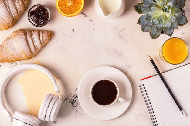 Blocco note, cuffie, croissant e caffè sul tavolo bianco