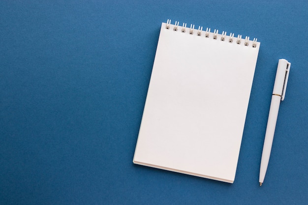Blocco note e penna in bianco su fondo blu scuro d'avanguardia. Notebook per idee, elenco e ispirazione. Vista dall'alto, piatto con spazio di copia. Mockup per il tuo design.