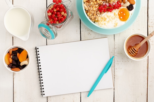 Blocco note per il piano di perdita di peso, prima colazione sana della ciotola di granola su di legno bianco