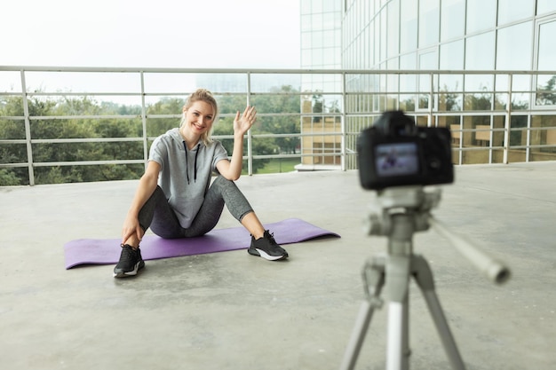 Blog di fitness. Giovane donna sportiva in buona salute che si registra sulla fotocamera con treppiede sul tetto dell'edificio, stile urbano. Vlogging