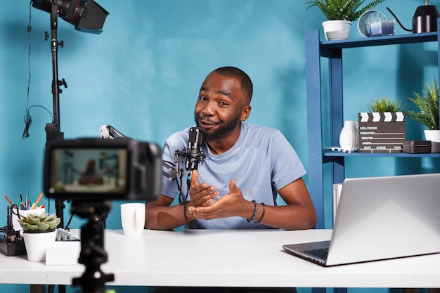 Blogger che guarda una telecamera professionale mentre filma contenuti digitali per il canale Internet. Creatore di contenuti Web che parla durante lo streaming e utilizza apparecchiature di vlogging nello studio di casa