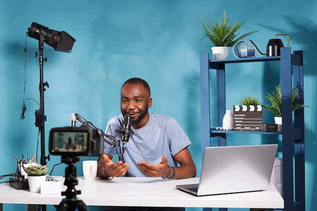 Blogger che utilizza fotocamera e microfono per lo streaming live sul canale dei social media. Video vlogger afroamericano che crea contenuti digitali con attrezzature professionali in studio