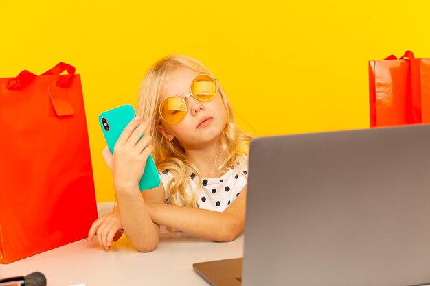 Blogger della bambina con il telefono blu che fa video per blog e seguaci che si siedono nello studio giallo isolato.