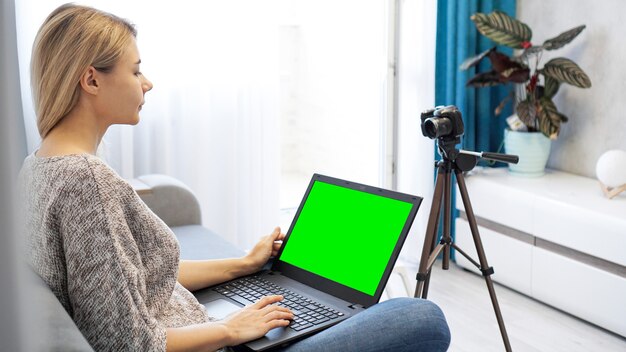 Blogger della donna che lavora al computer portatile. Vista della fotocamera su treppiede e laptop con chromakey schermo verde