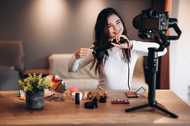 Blogger di bellezza bella femmina che filma tutorial di routine di trucco quotidiano sulla macchina fotografica. Influencer giovane donna live streaming recensione di prodotti cosmetici in home studio. Lavoro da vlogger. Fai da te mettendo il trucco.