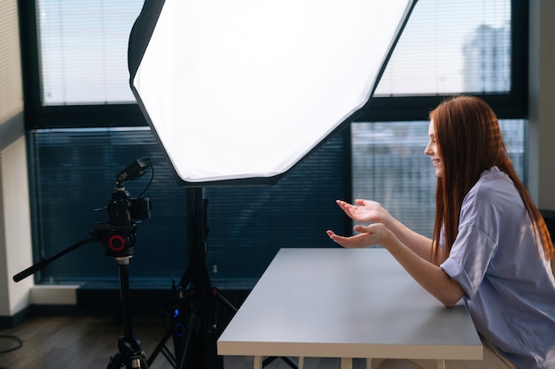 Blogger di successo giovane donna che registra video vlog utilizzando la fotocamera e il softbox seduto alla scrivania