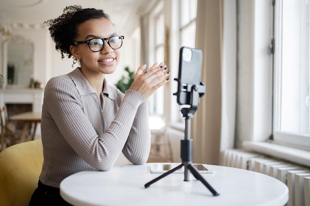 Blogger femminile con occhiali video chat con i colleghi di una società finanziaria in ufficio utilizza il telefono