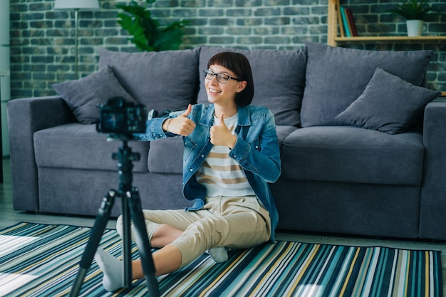 Blogger femminile di successo che registra video con una fotocamera moderna che mostra il pollice in su