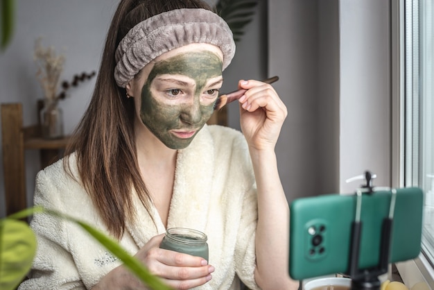 Blogger sta applicando una maschera cosmetica verde sul viso su un telefono cellulare