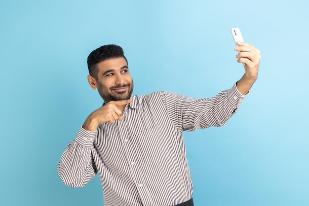 Blogger uomo bello con la barba che punta il dito sulla fotocamera del telefono che fa selfie o registra video