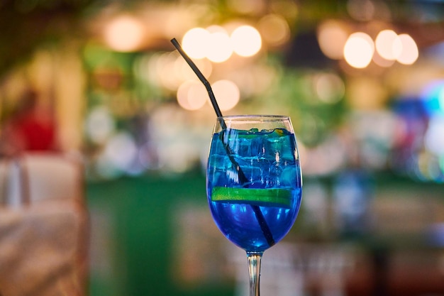 Blue Lagoon cocktail in vetro con paglia, spazio per la copia del fondo del bokeh della luce del caffè di notte. Gustoso cocktail blu sul tavolino del bar. Liquore blu Curacao con vodka aromatizzata e limonata