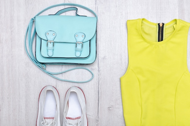 Blusa verde chiaro, sneakers bianche e borsa a mano. Concetto alla moda. Fondo in legno.