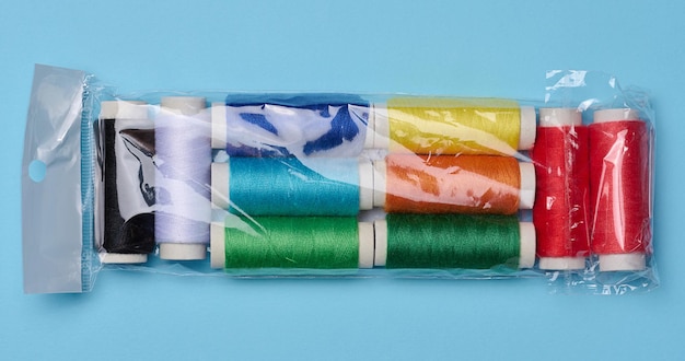 Bobine multicolori di fili per cucire in un sacchetto di plastica su sfondo blu vista dall'alto