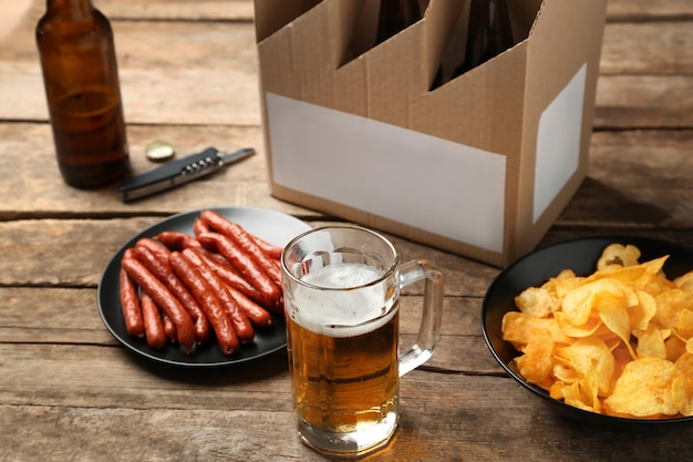 Boccale di birra con snack e pacchetto di carta su sfondo di legno