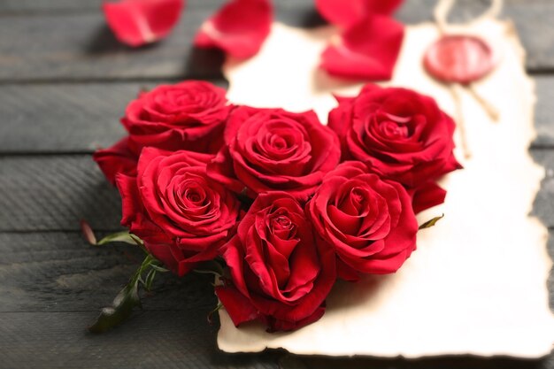 Boccioli di rose rosse fresche a forma di cuore con carta presente in bianco su fondo di legno