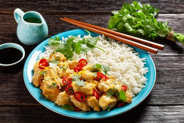 Bocconcini di petto di pollo speziati glassati al mango con riso su un piatto blu con le bacchette su un tavolo di legno scuro vista orizzontale dall'alto