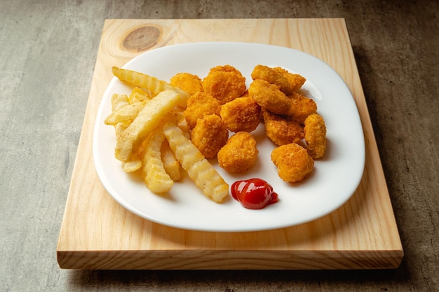 Bocconcini di pollo e patatine fritte con un po' di salsa di pomodoro su un piatto su una superficie di legno pronto da mangiare pasto veloce