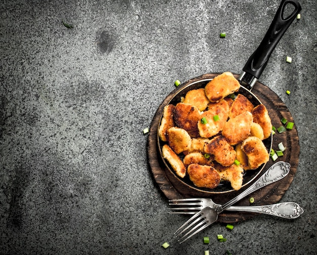 Bocconcini di pollo in padella. Su fondo rustico.