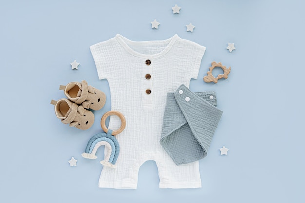 Body bianco in cotone con scarpine e giocattoli. Set di vestiti e accessori per bambini su sfondo blu. Vestiti alla moda per neonati per l'estate. Disposizione piatta, vista dall'alto