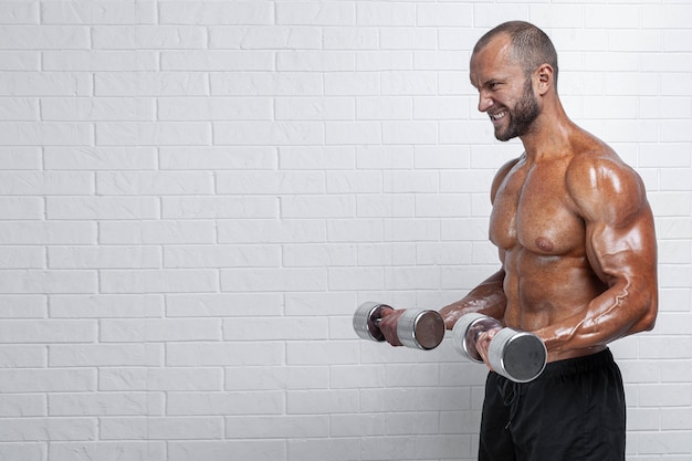 Bodybuilder facendo esercizi per bicipiti con manubri contro il muro di mattoni.