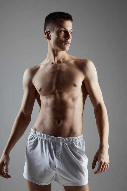 Bodybuilder maschio in pantaloncini corti che fa gesti con le mani su uno sfondo grigio Foto di alta qualità