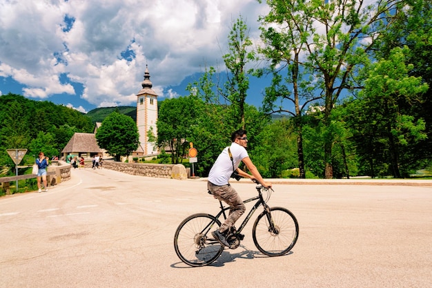 Bohinj, Slovenia - 3 giugno 2019: Uomo in bicicletta nella Chiesa di San Giovanni Battista sul lago di Bohinj in Slovenia. Paesaggio, paesaggio urbano e natura in Slovenia. Vista del cielo blu con nuvole, estate.