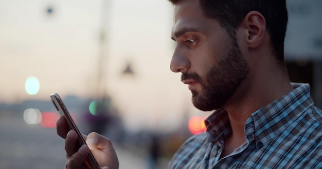 Bokeh primo piano dell'uomo indiano che utilizza lo smartphone sulla strada della città