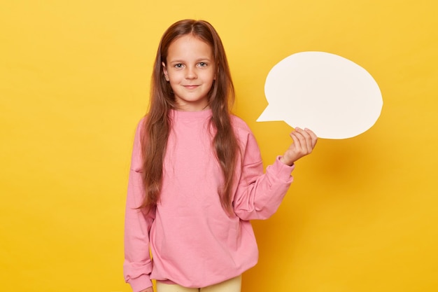 Bolla di discorso creativa per la comunicazione Spazio vuoto Ragazza sorridente con i capelli lunghi che tiene in mano una bolla di discorsi vuota che indossa una felpa rosa isolata su uno sfondo giallo