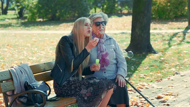 Bolle di salto della giovane donna felice che si siedono insieme a sua nonna in parco