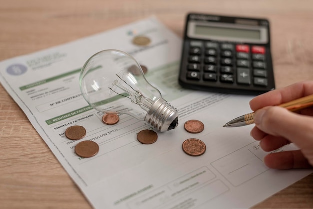 Bolletta elettrica con lampadina Calcolatrice di diverse monete e una penna che tiene la mano sulla scrivania Concetto di prezzi dell'elettricità e pagamento delle tasse