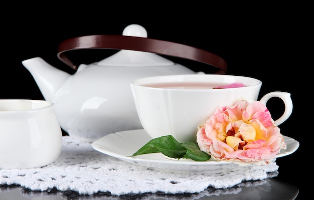 Bollitore e tazza di tè dalla rosa tea su sfondo nero tovagliolo