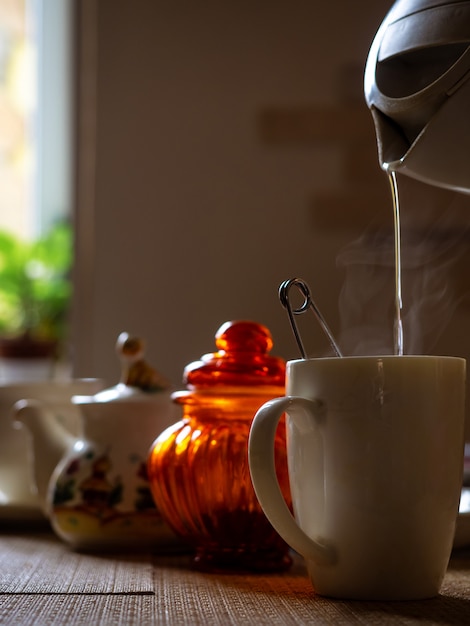 Bollitore versa acqua calda al mattino con vapore in una tazza