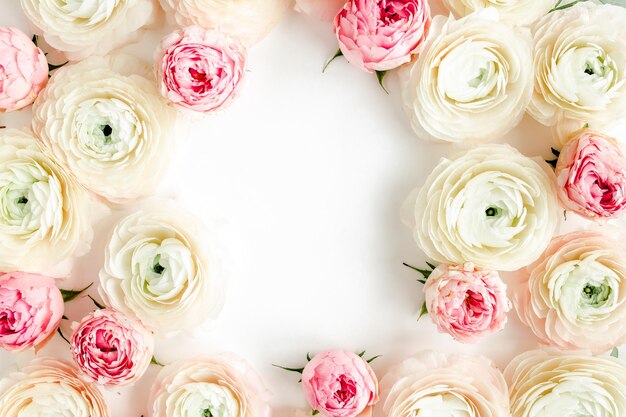 Bordi della cornice floreale realizzati in ranuncolo rosa e boccioli di fiori di rose su sfondo bianco Sfondo floreale con vista dall'alto piatta