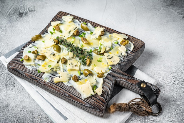 Bordo di burro con erbe capperi di formaggio blu parmigiano e olive Butterboard Sfondo bianco Vista dall'alto