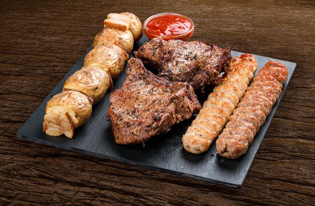 Bordo di pietra con carne cotta saporita differente su fondo di legno Patate di lyulya del kebab di vitello