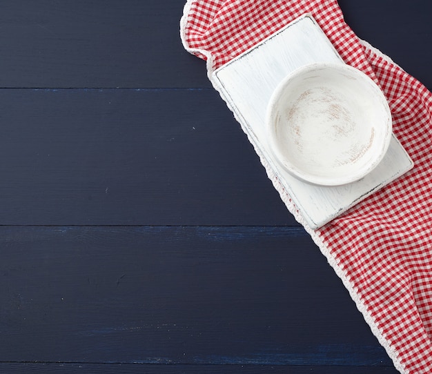 Bordo rettangolare bianco della cucina di taglio e piatto rotondo vuoto su una superficie di legno blu