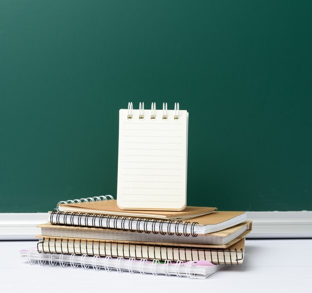 Bordo scolastico di gesso verde vuoto e pila di quaderni, torna a scuola, copia dello spazio