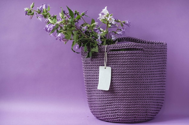Borsa a maglia viola fatta a mano con fiori su sfondo viola. Copia, spazio vuoto per il testo
