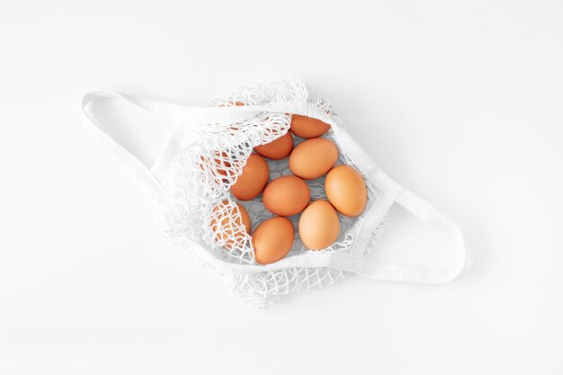 Borsa a rete bianca con uova marroni piatte adagiate su sfondo bianco vista dall'alto spazio copia. Borsa per la spesa ecologica e riutilizzabile. Borsa a tracolla in maglia di cotone. Zero rifiuti concetto di pasqua. Giorno di Pasqua in stile minimalista