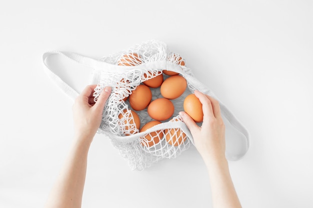 Borsa a rete bianca con uova marroni piatte adagiate su sfondo bianco vista dall'alto spazio copia. Borsa per la spesa ecologica e riutilizzabile. Borsa a tracolla in maglia di cotone. Zero rifiuti concetto di pasqua. Giorno di Pasqua in stile minimalista