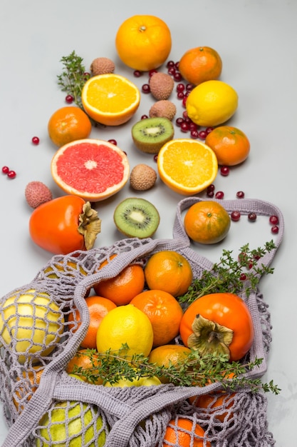 Borsa a rete riutilizzabile con frutta. Mandarini, pompelmi, kiwi, uva e foglie di bietola sul tavolo.
